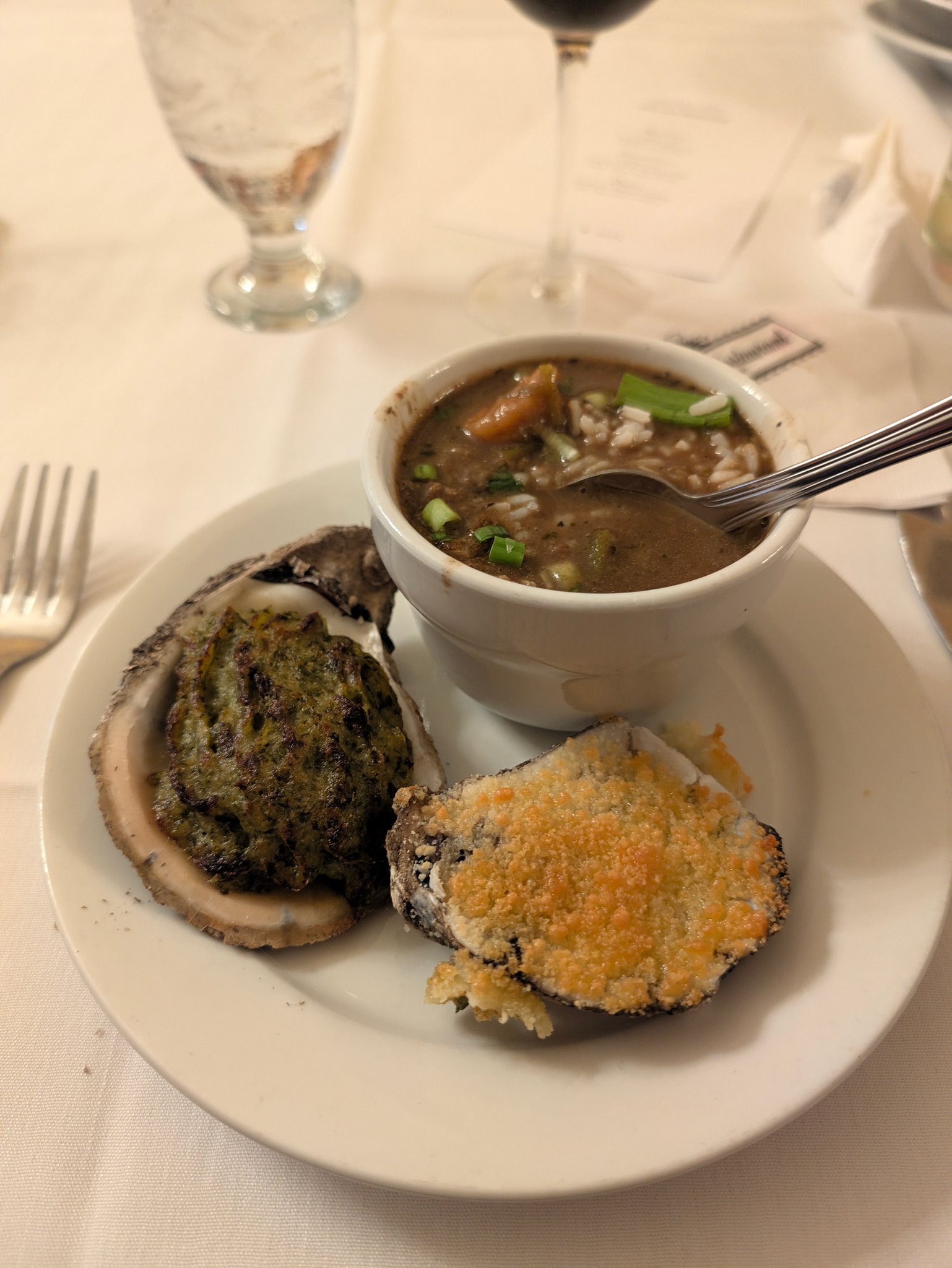 Cup of gumbo with green onions served alongside baked oysters on a plate at Antoine's in New Orleans