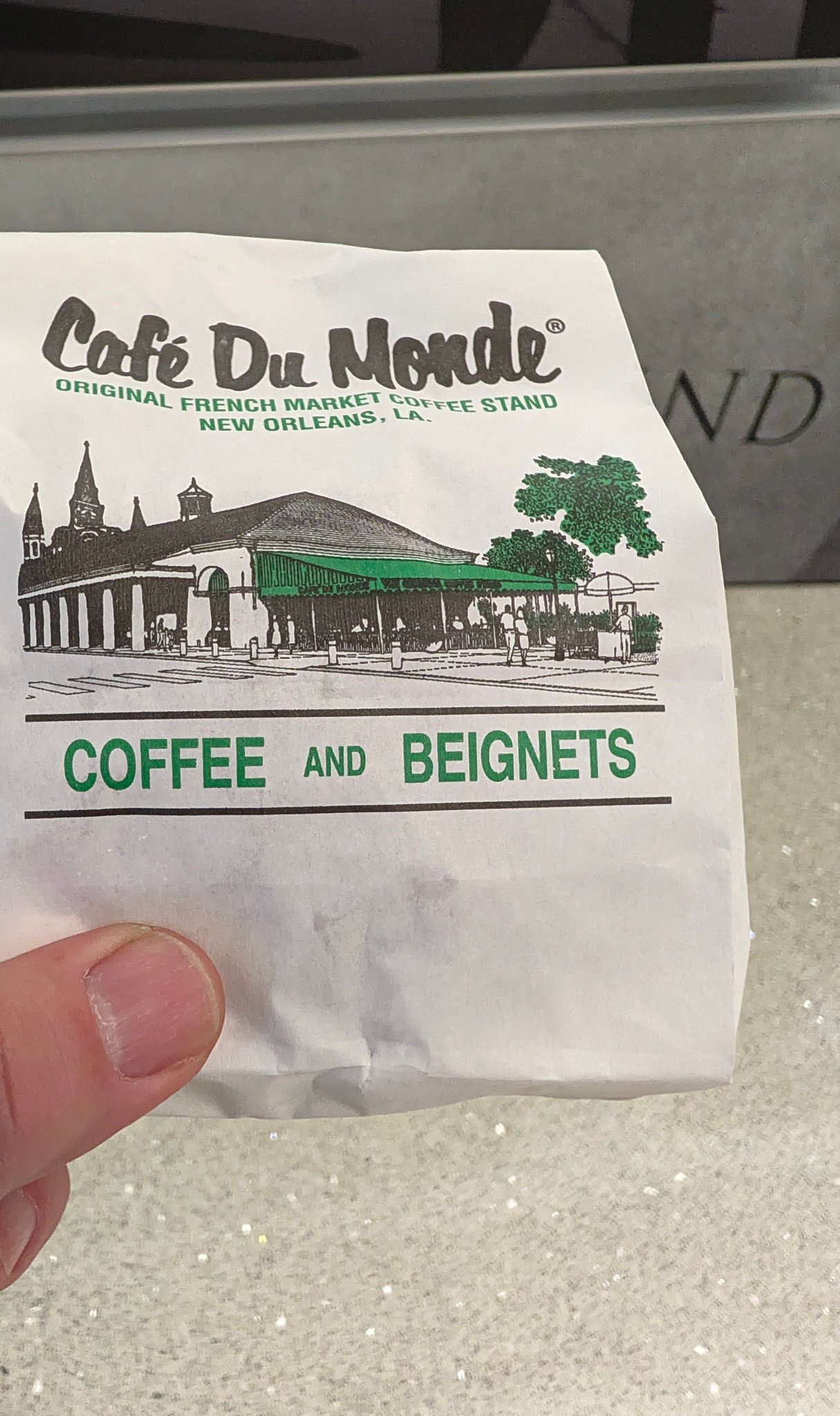 Hand holding a Cafe du Monde coffee and beignets bag at the New Orleans airport location