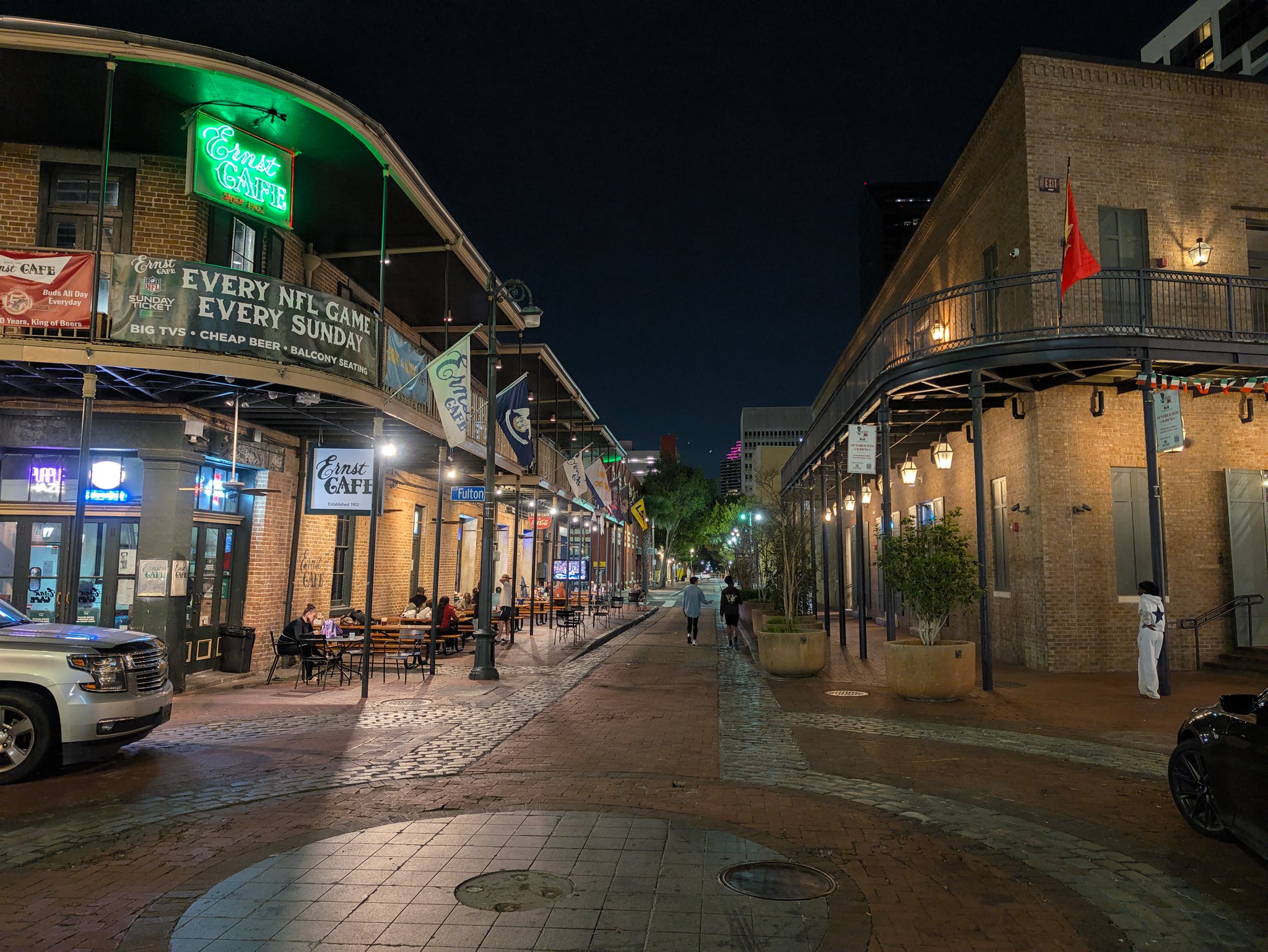 Green neon Ernst Cafe sign over a brick building and a quiet street at night in New Orleans
