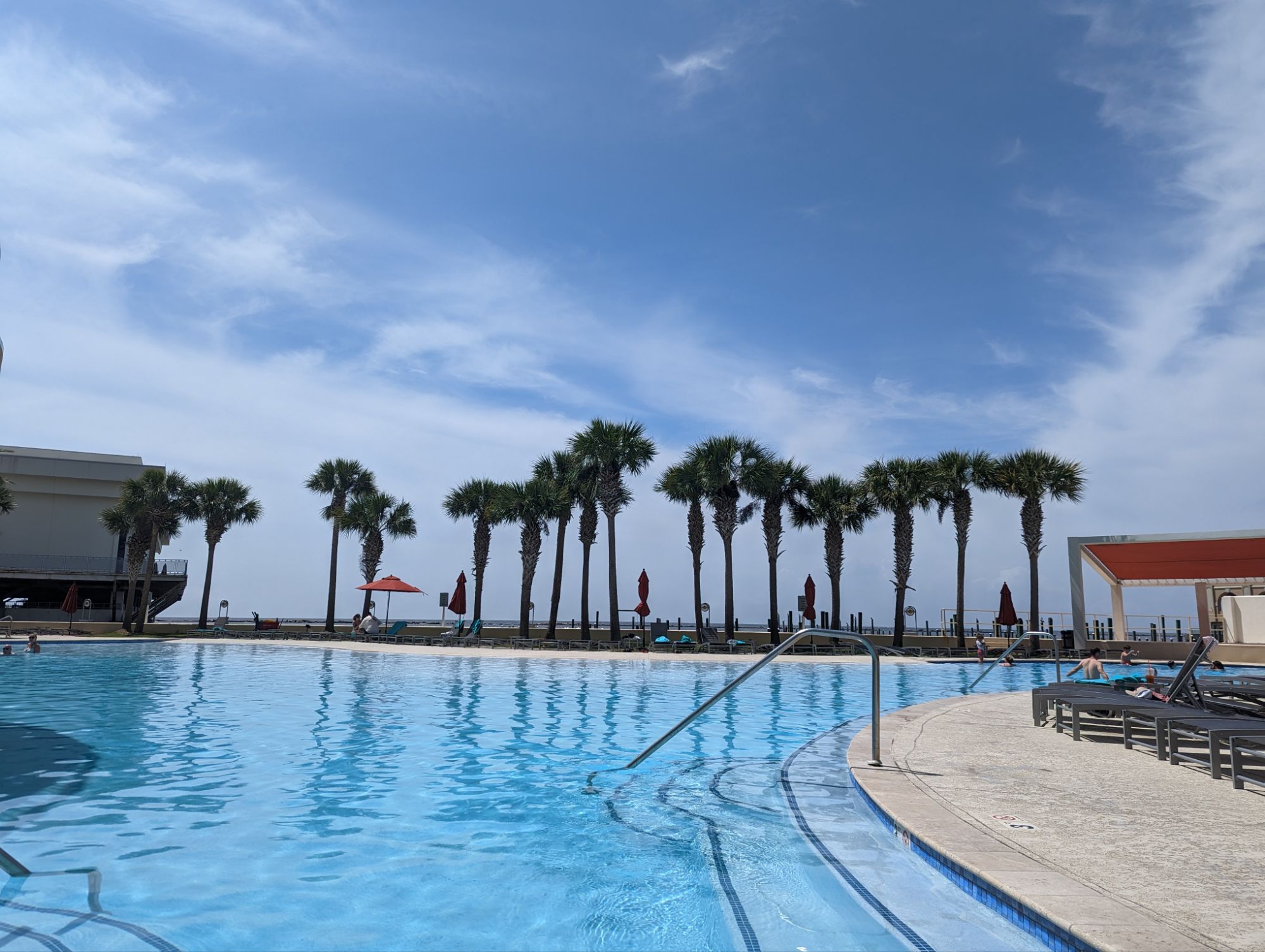 Palm-lined pool deck with red umbrellas at Hard Rock Hotel & Casino Biloxi