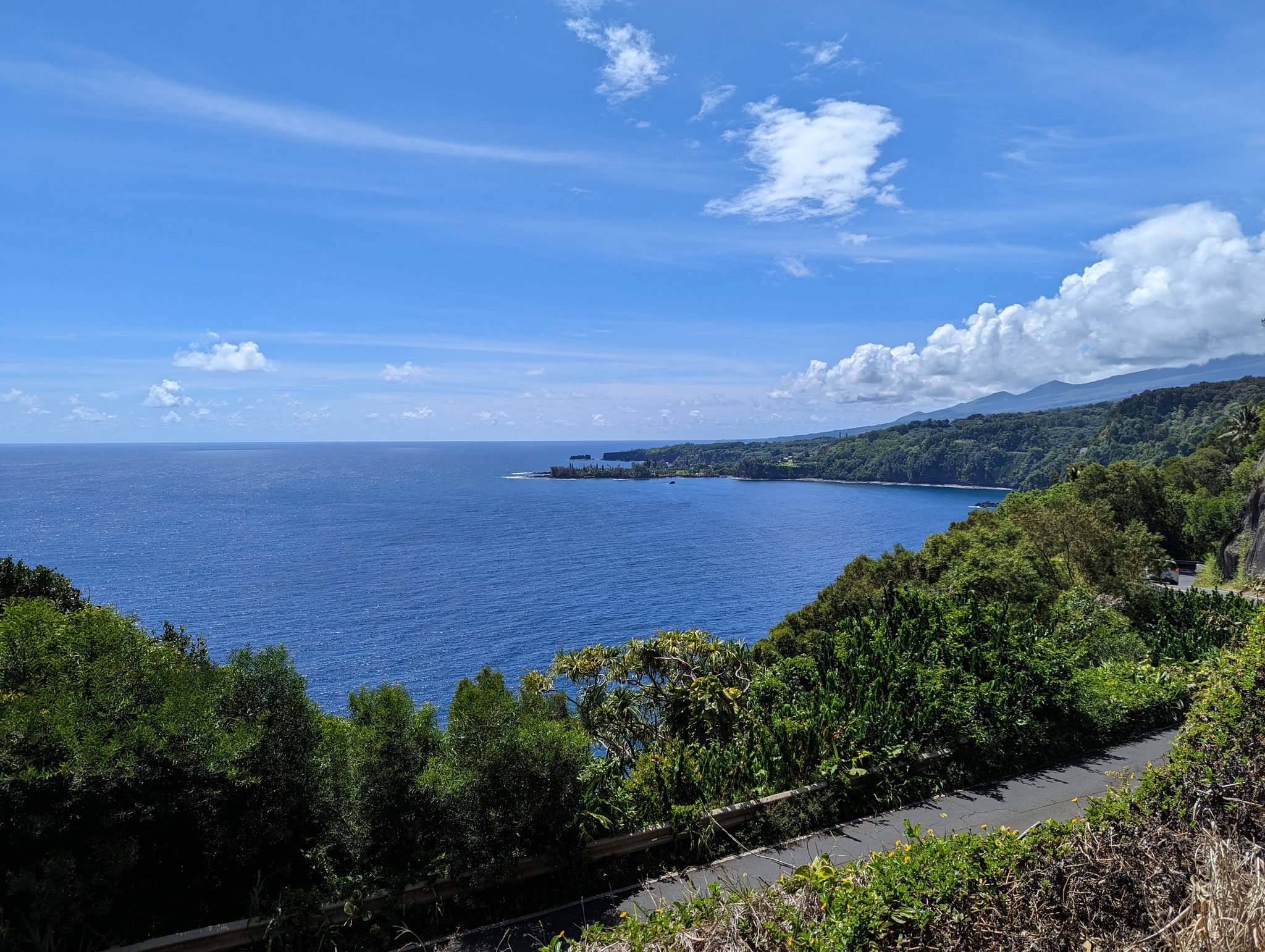 Wide view of deep blue ocean and green coastline from a roadside overlook on the Road to Hana, Maui