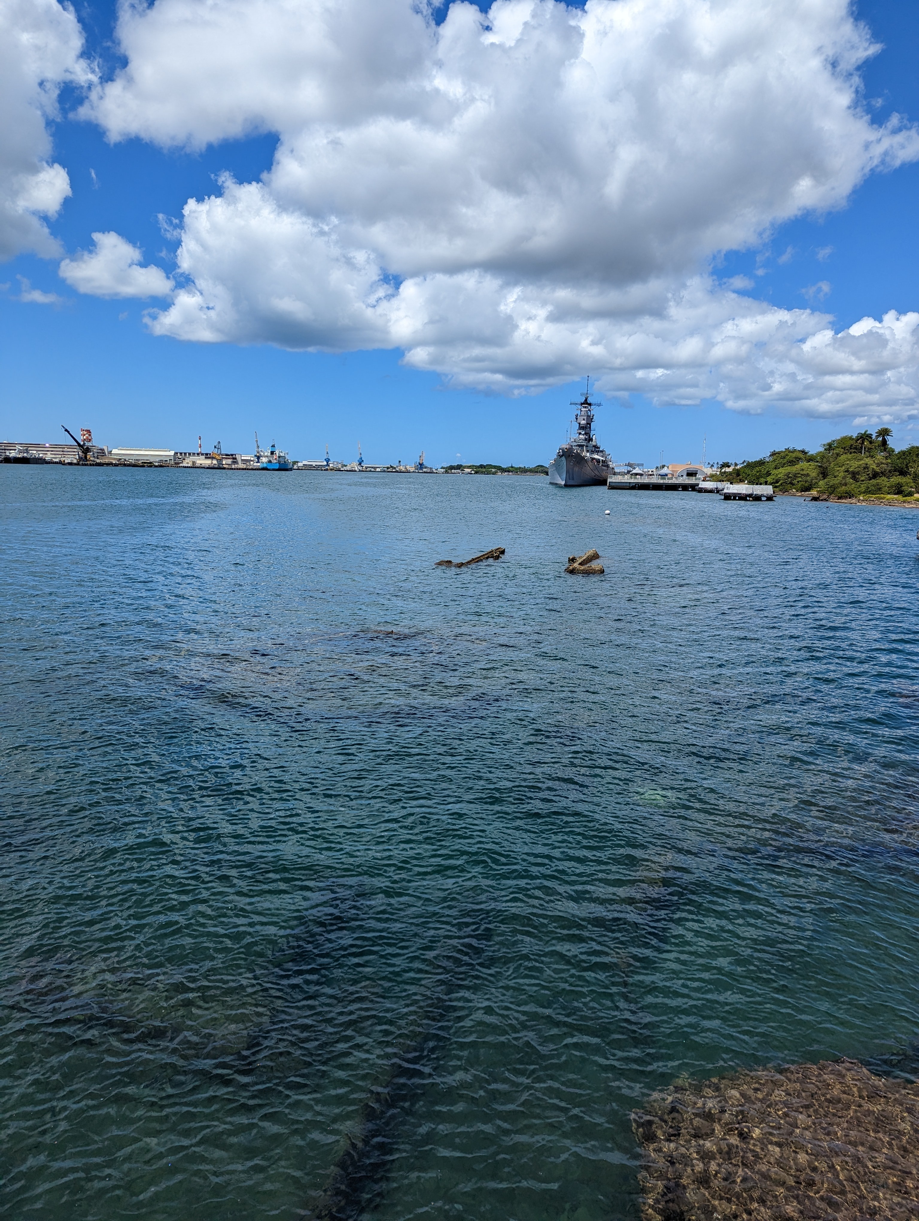 The sunken USS Arizona beneath the water at Pearl Harbor, with the USS Missouri in the distance
